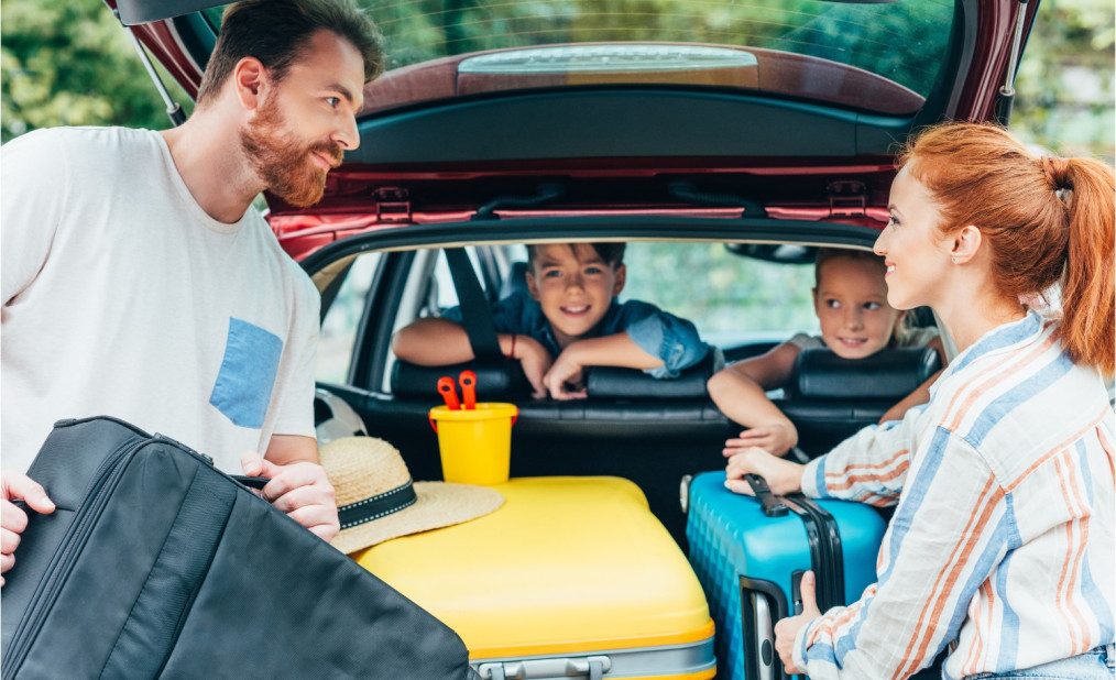 family of four packing suitcases into the back of the car, preparing for a family trip
