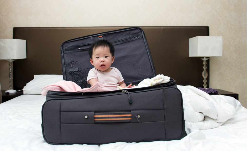 toddler sitting in a suitcase on hotel bed