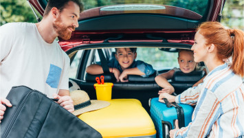 family of four packing suitcases into the back of the car, preparing for a family trip