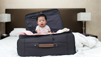 toddler sitting in a suitcase on hotel bed