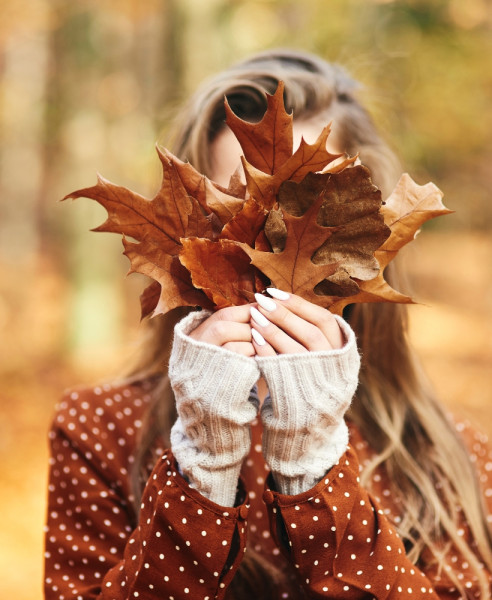 woman holding autumn leaf in front of her face